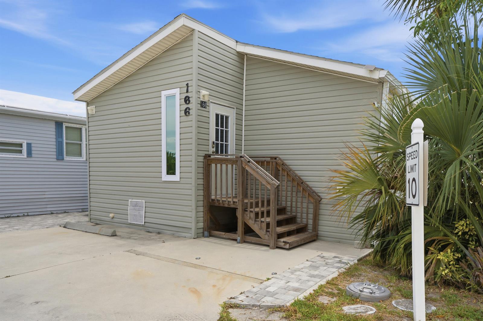 A light green mobile home with a wooden staircase and a speed limit sign outside — 166 Nettles Boulevard, Jensen Beach FL 34957, JENSEN BEACH, FL
