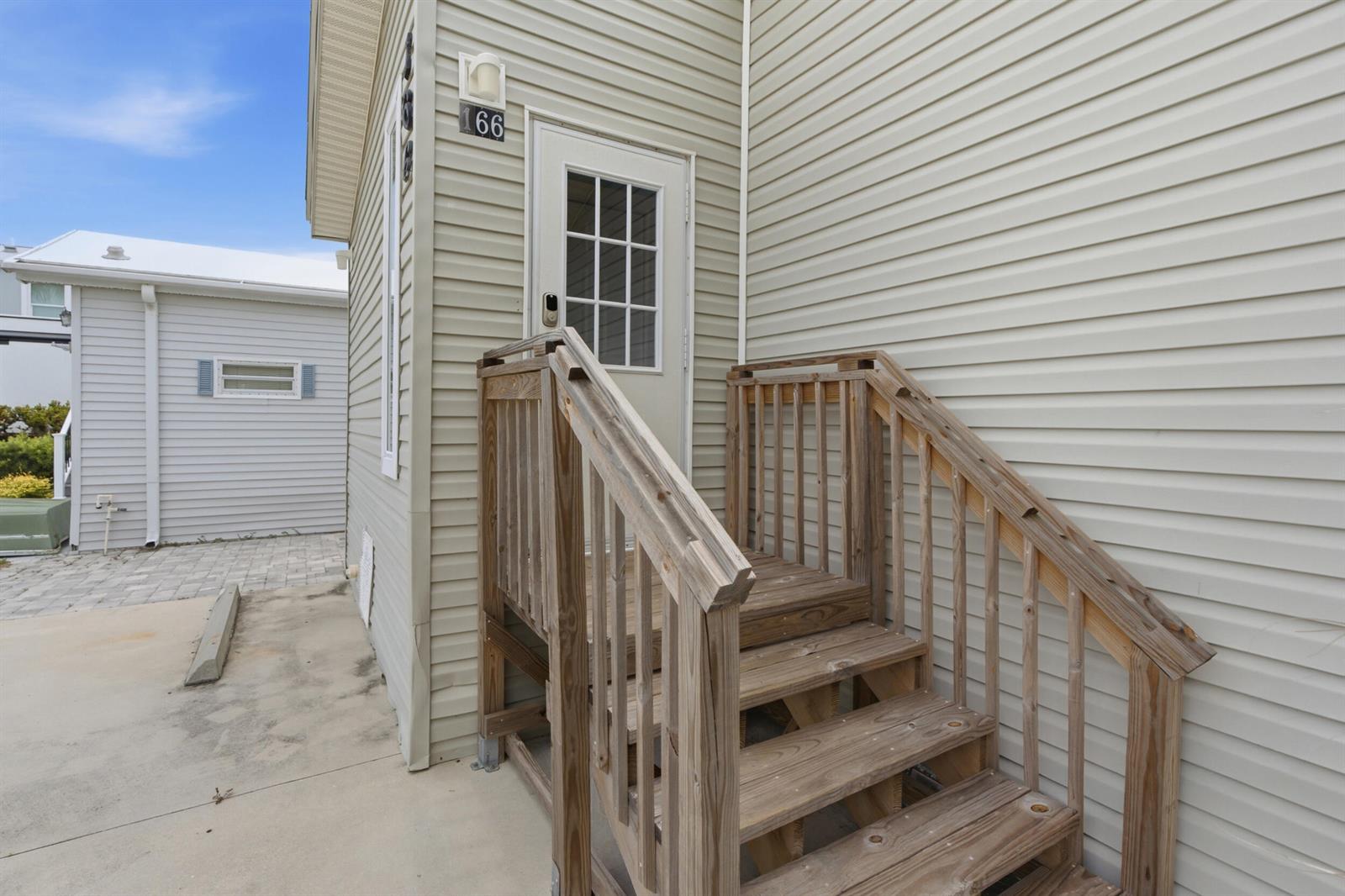 A wooden staircase leads to the white door of a house with light-colored siding — 166 Nettles Boulevard, Jensen Beach FL 34957, JENSEN BEACH, FL