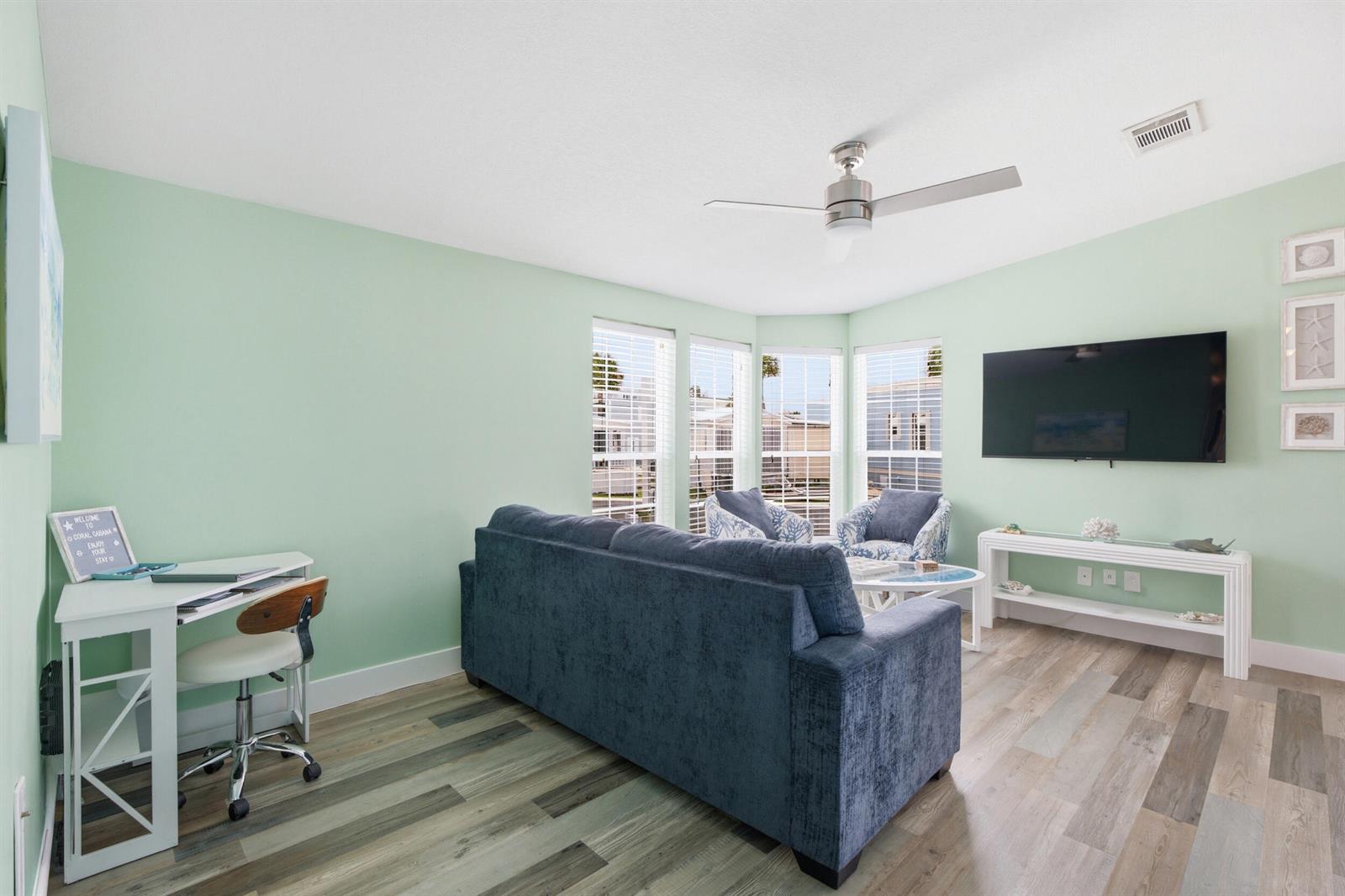 A living room with light green walls, a blue sofa, a desk, and a television — 166 Nettles Boulevard, Jensen Beach FL 34957, JENSEN BEACH, FL