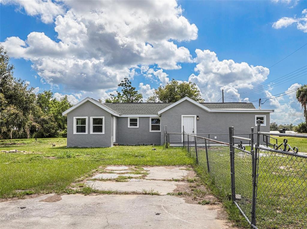 A gray, single-story house with a chain-link fence and a concrete driveway in front — 205 E CORNELL STREET, AVON PARK, FL