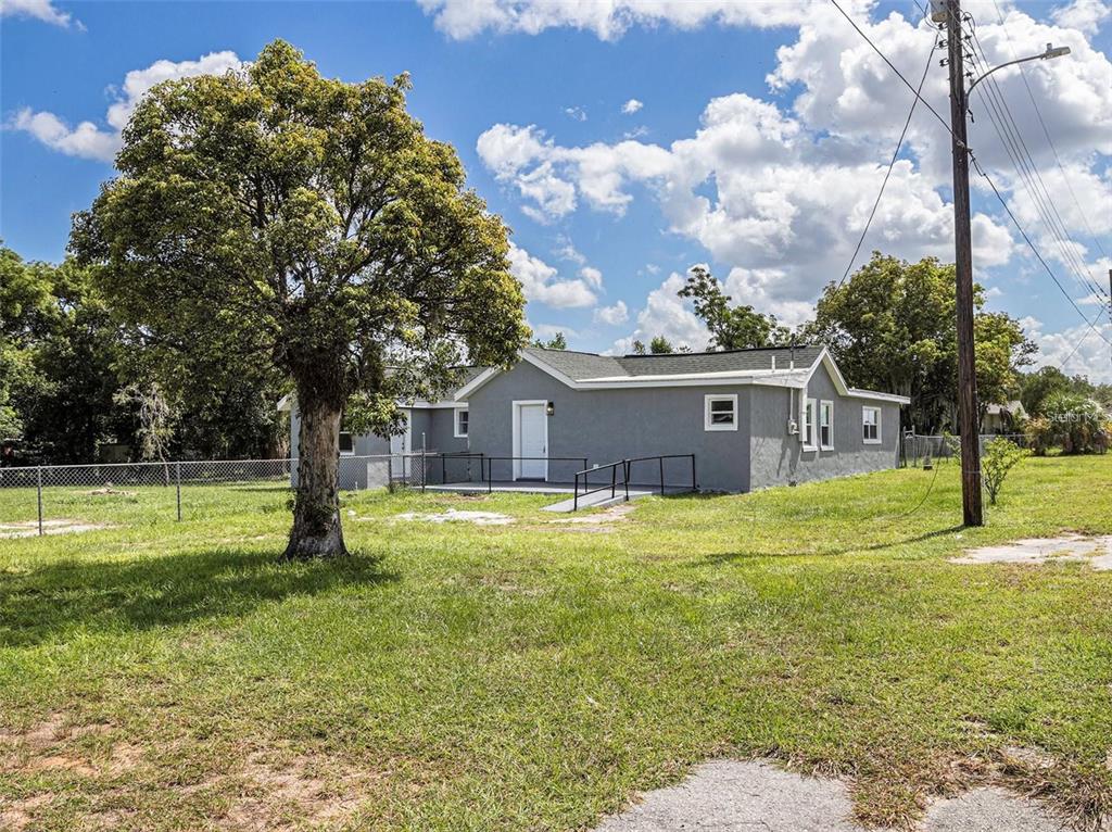 A gray, single-story house with a wheelchair ramp sits on a grassy lot — 205 E CORNELL STREET, AVON PARK, FL
