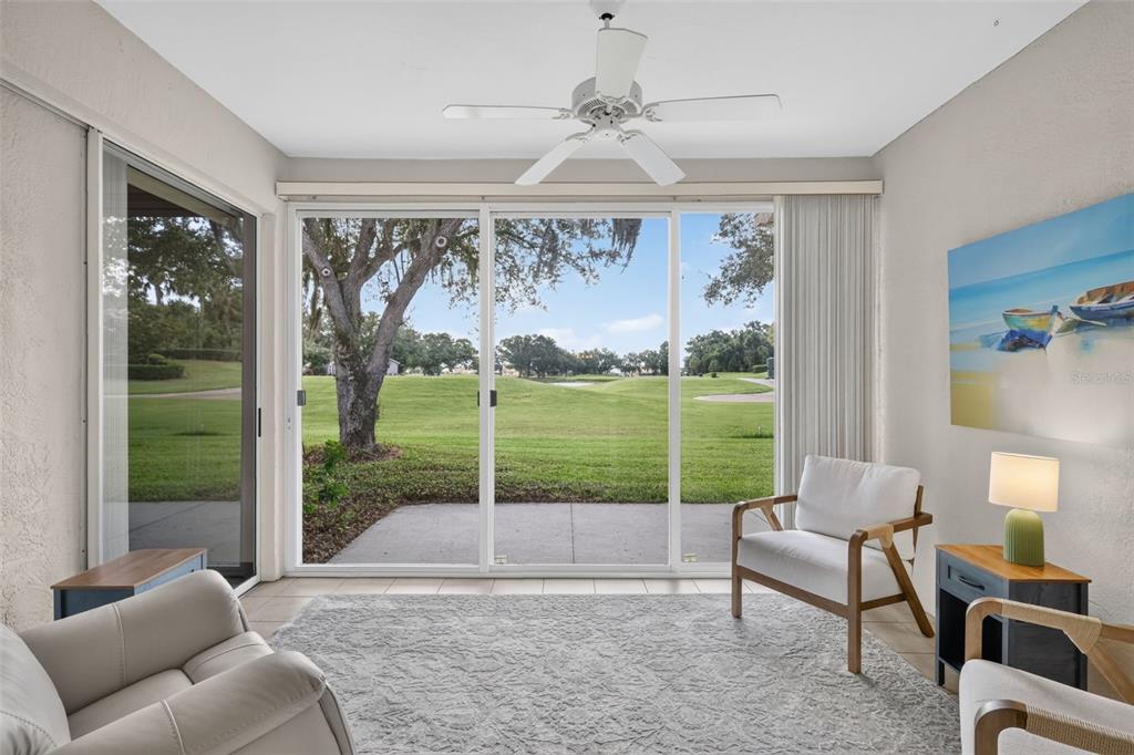 A sunroom features a ceiling fan, large sliding glass doors, and a view of a golf course — 6314 STONE RIVER ROAD, BRADENTON, FL