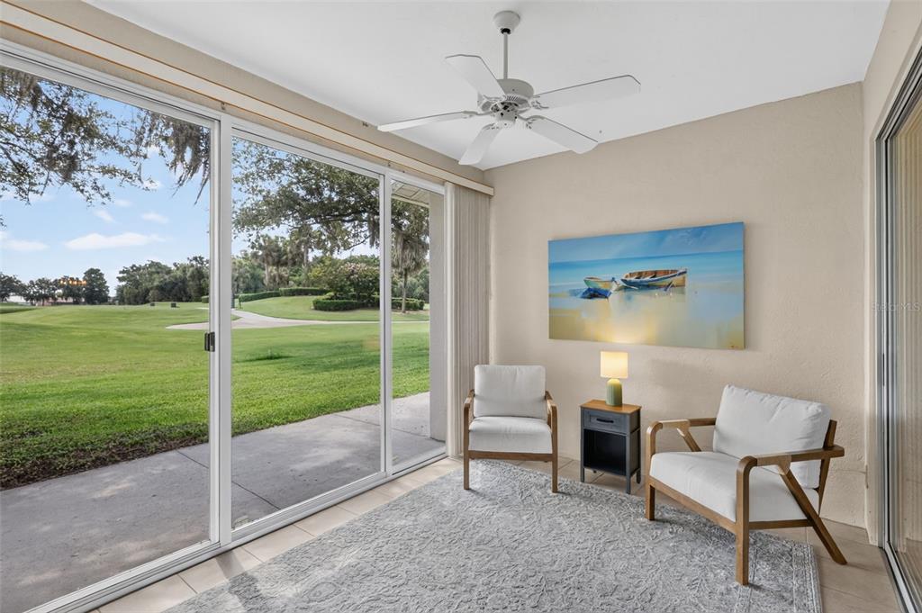 A sunroom features two white armchairs, a small side table, and sliding glass doors overlooking a golf course — 6314 STONE RIVER ROAD, BRADENTON, FL