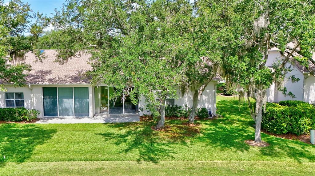 A rear view of a single-story house with a sliding glass door and large trees — 6314 STONE RIVER ROAD, BRADENTON, FL