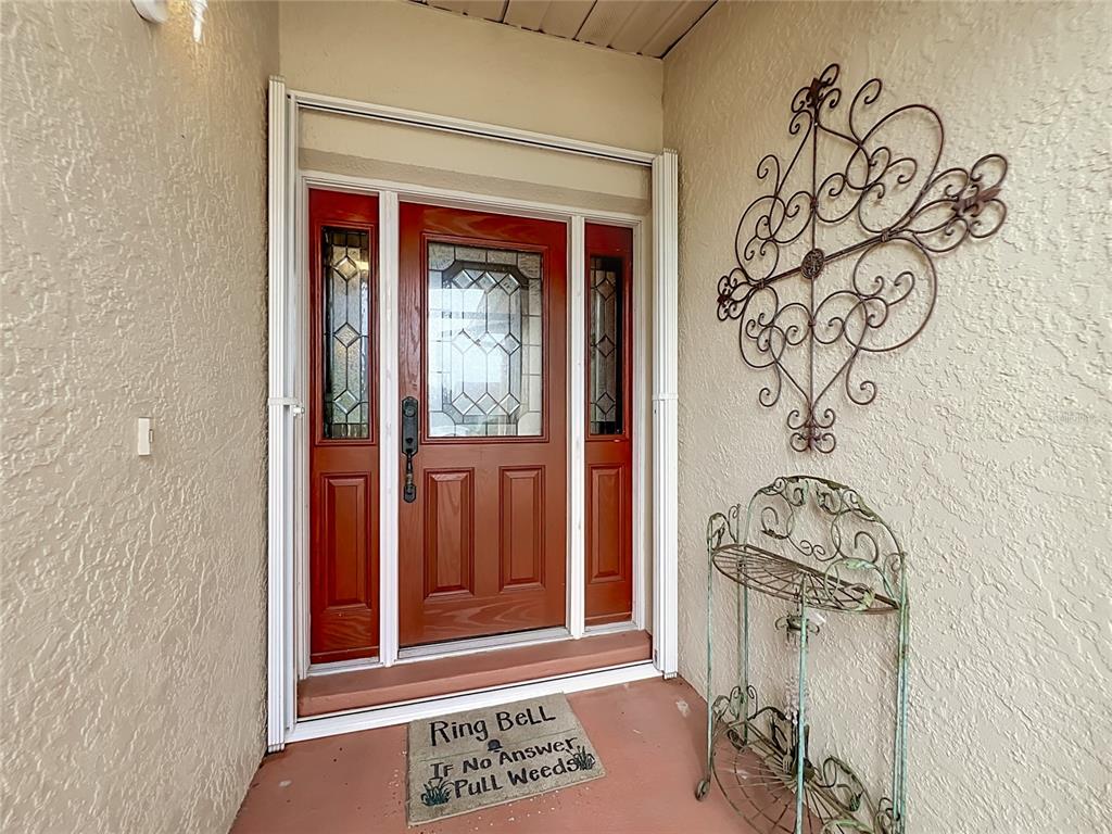A red front door with glass panels sits under a covered entryway with wall decor — 859 YORKTOWNE DRIVE, ROCKLEDGE, FL