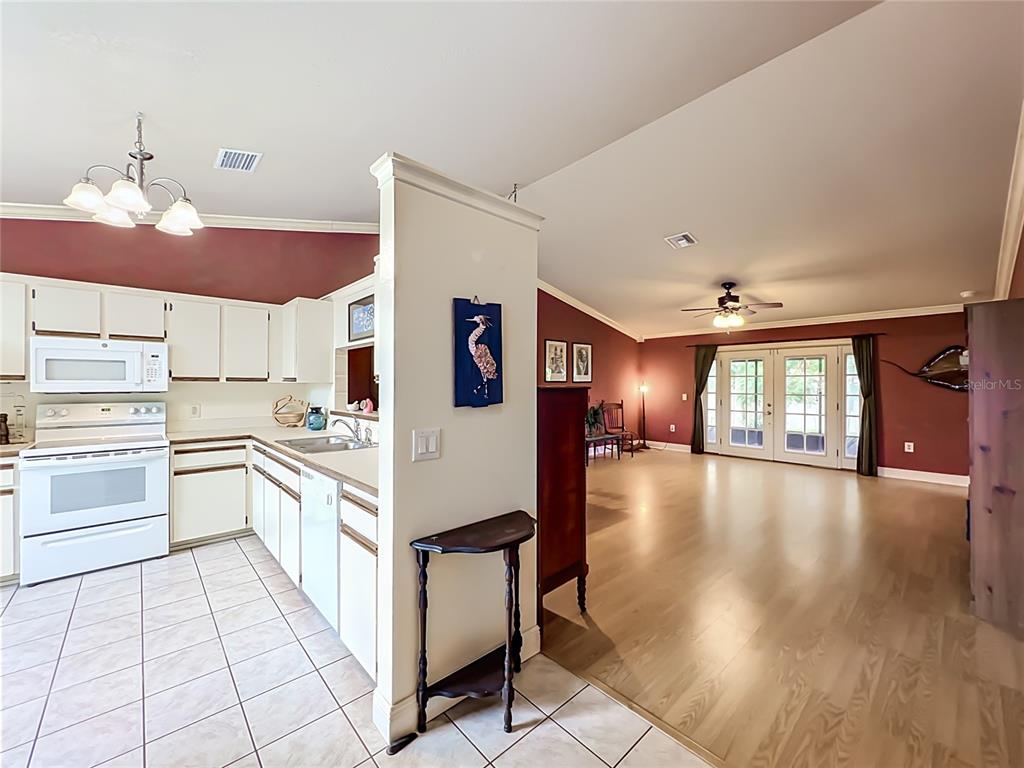 A kitchen with white cabinets and tile flooring opens into a living room with wood floors — 859 YORKTOWNE DRIVE, ROCKLEDGE, FL