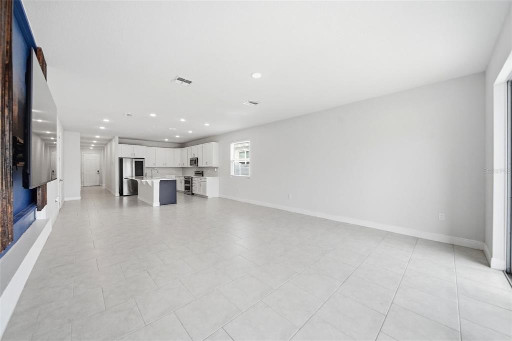 A spacious, open-concept living area features light tile flooring, white walls, and a modern kitchen — 1120 MATTIE POINTE BOULEVARD, AUBURNDALE, FL