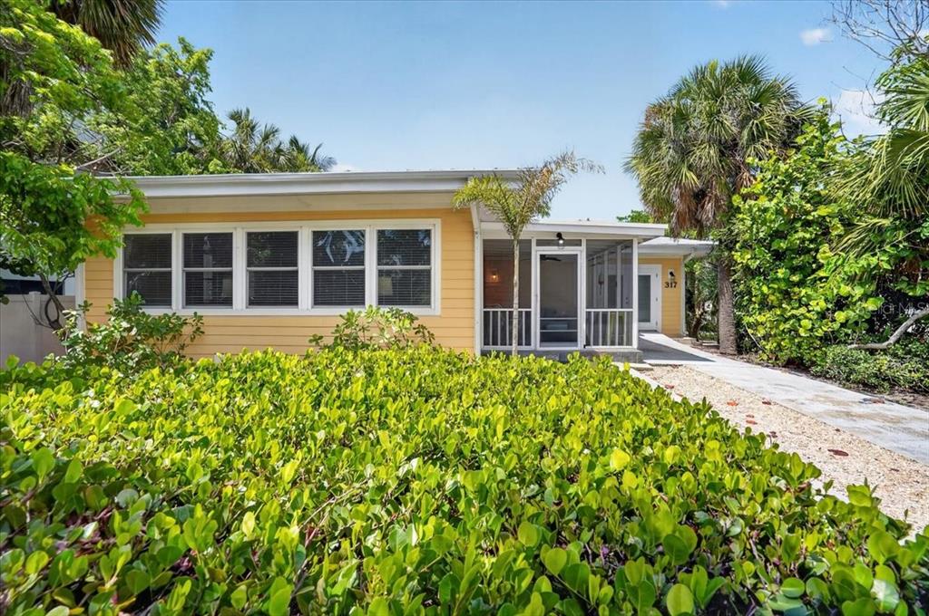 A yellow single-story house with a screened porch and lush landscaping in the front yard — 317 N BAY BOULEVARD, ANNA MARIA, FL