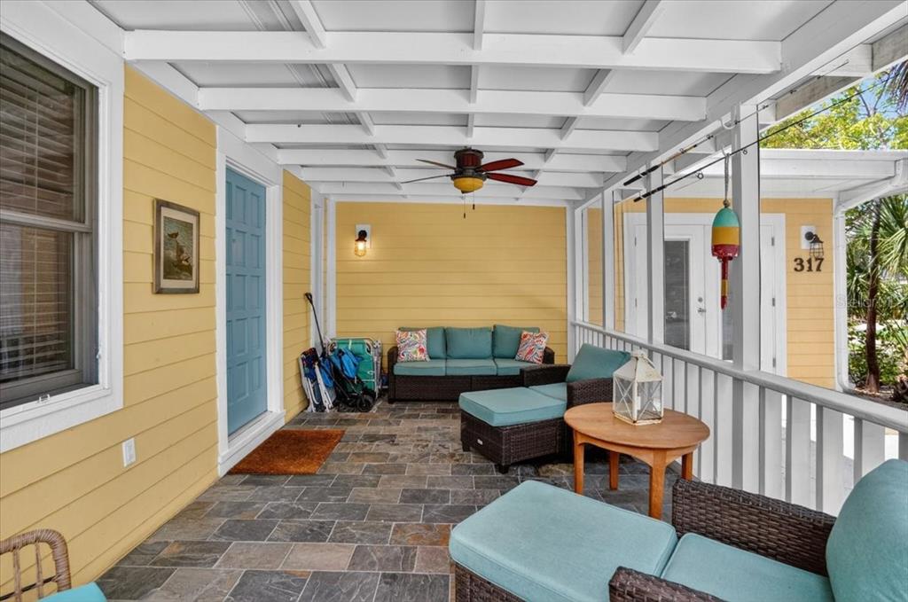 A covered porch with yellow siding, stone flooring, wicker furniture, and a ceiling fan — 317 N BAY BOULEVARD, ANNA MARIA, FL