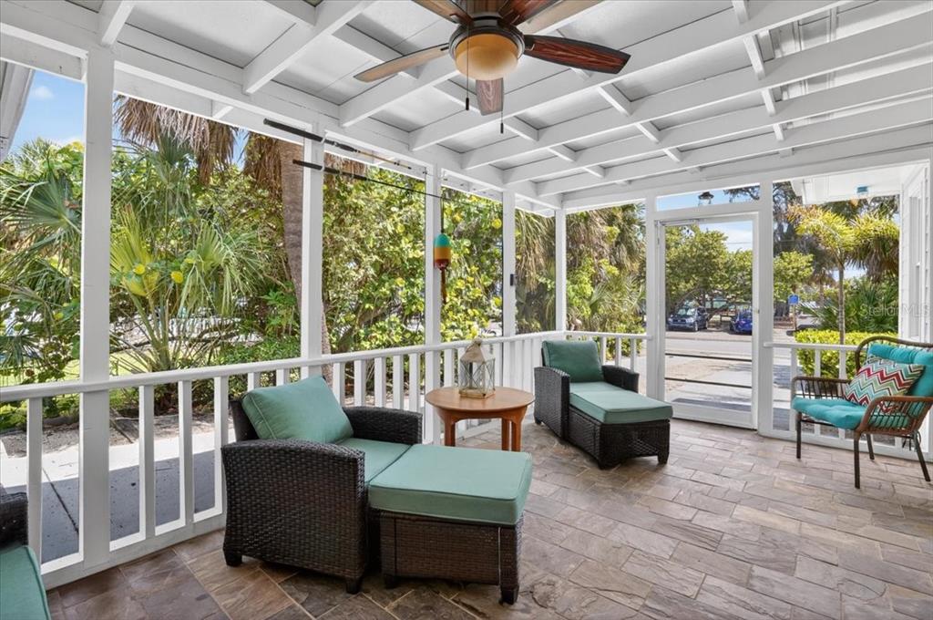 A screened-in porch features wicker furniture, a ceiling fan, and a view of outdoor greenery — 317 N BAY BOULEVARD, ANNA MARIA, FL