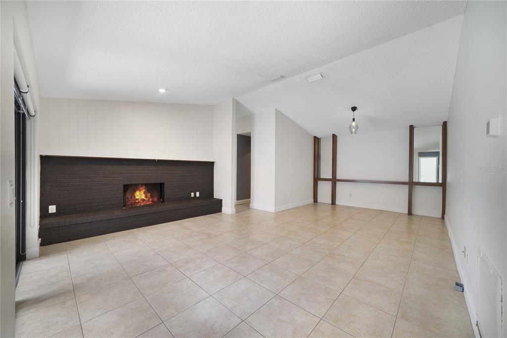 A living room features a black brick fireplace, tile flooring, and vaulted ceilings — 5025 BERMUDA CIRCLE UNIT 5025, ORLANDO, FL