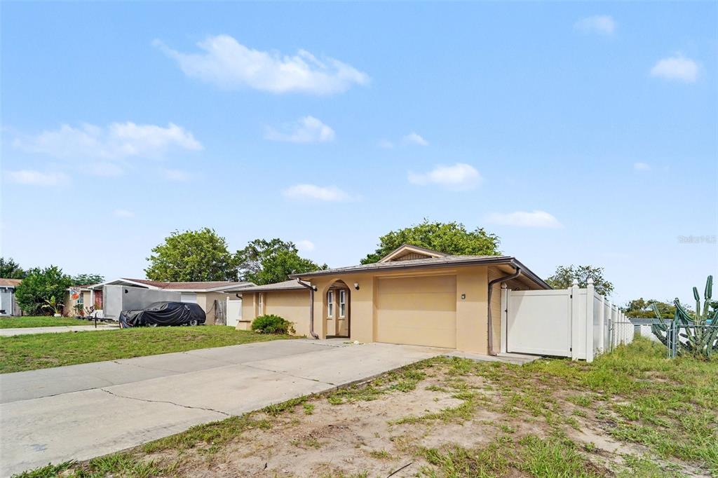 A single-story house with a tan exterior, a concrete driveway, and a white privacy fence — 7612 DALE DRIVE, PORT RICHEY, FL