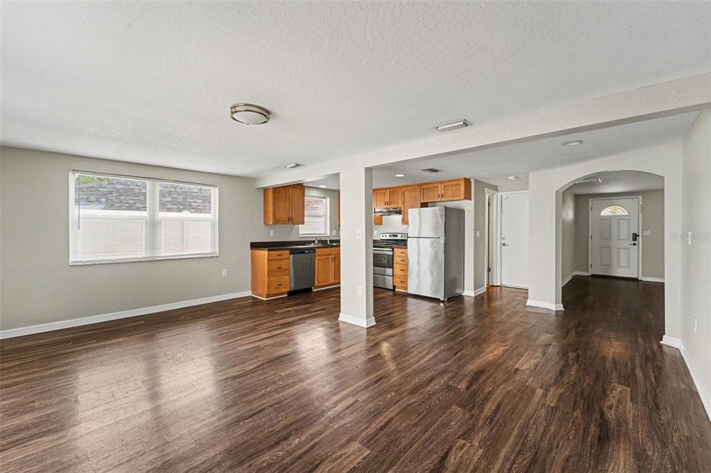 An open-concept living area features wood-look flooring, a kitchen with wood cabinets, and stainless appliances — 7612 DALE DRIVE, PORT RICHEY, FL