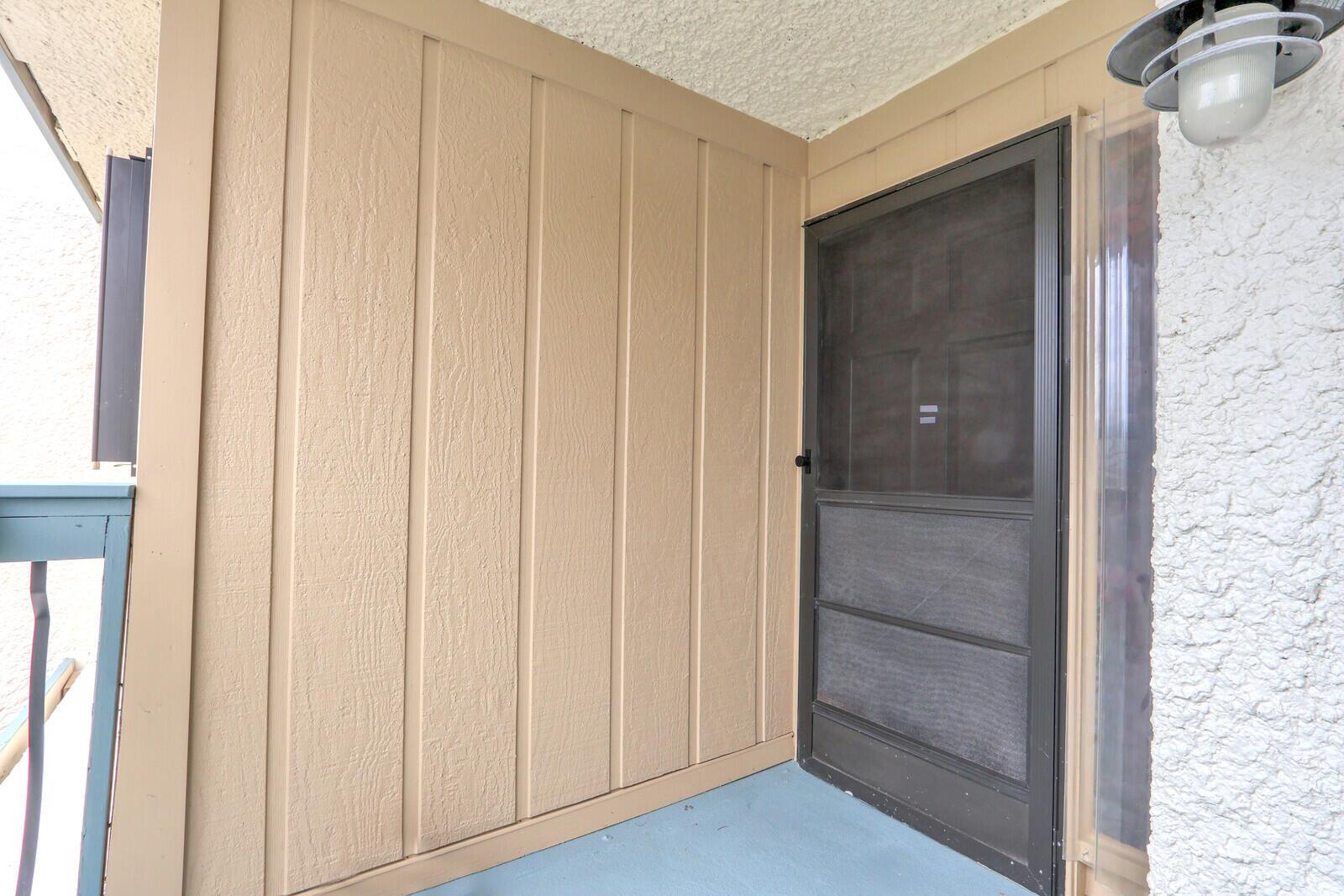A tan-sided exterior wall with a dark screen door and a light fixture above — 1551 NE 13th Terrace # A9, Jensen Beach FL 34957, JENSEN BEACH, FL
