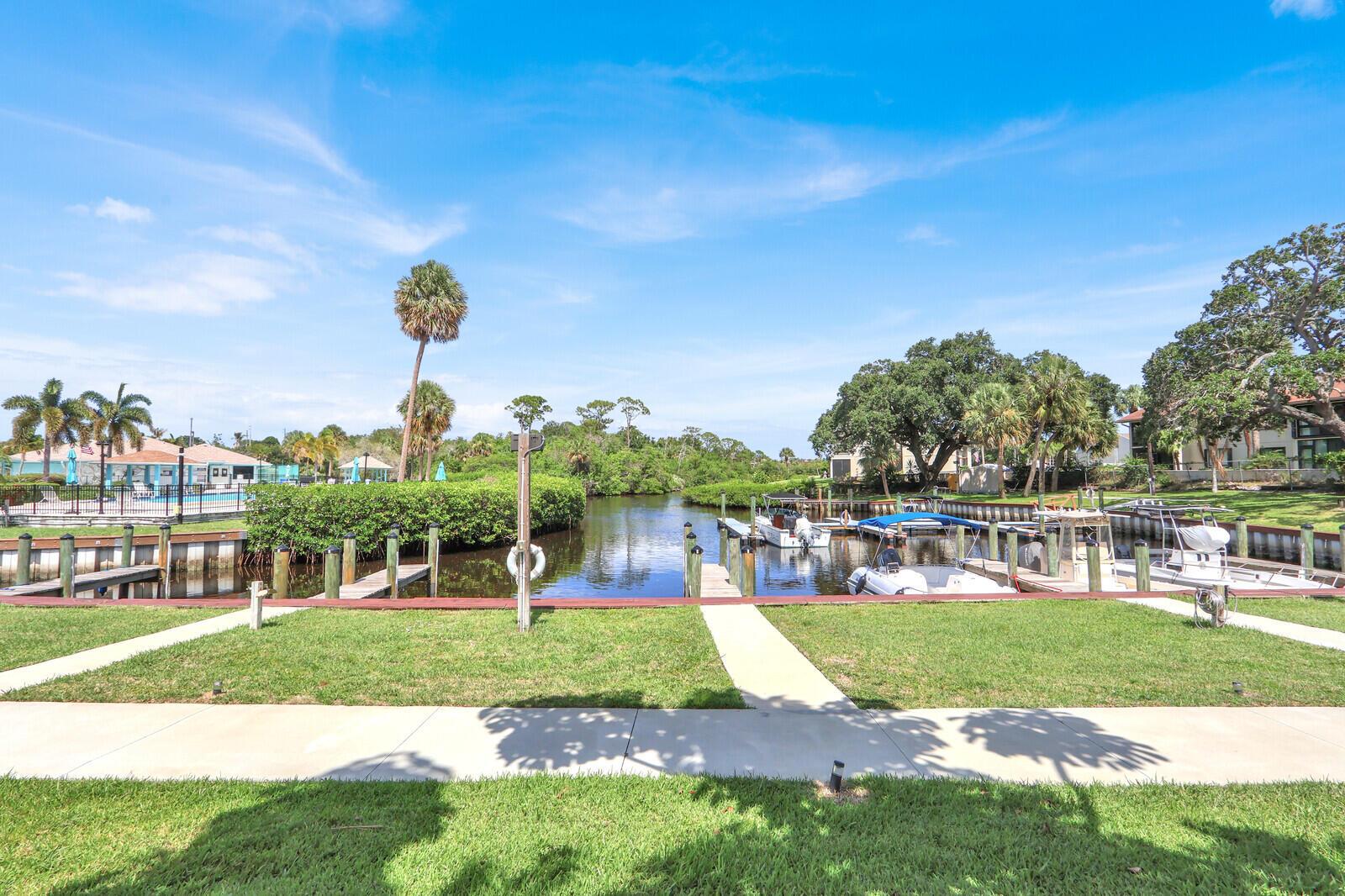 A view of a canal with boat slips, a grassy lawn, and palm trees — 1551 NE 13th Terrace # A9, Jensen Beach FL 34957, JENSEN BEACH, FL