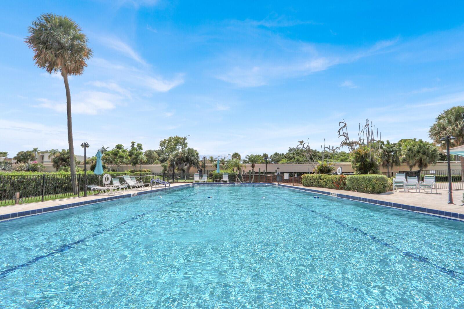 A rectangular outdoor swimming pool is surrounded by a patio, lounge chairs, and palm trees — 1551 NE 13th Terrace # A9, Jensen Beach FL 34957, JENSEN BEACH, FL
