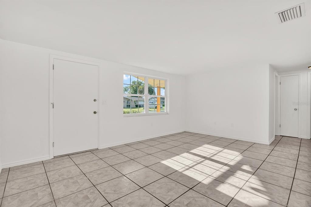 An empty room with white walls, tiled floors, a single window, and two white doors — 6701 PARKSIDE DRIVE, NEW PORT RICHEY, FL