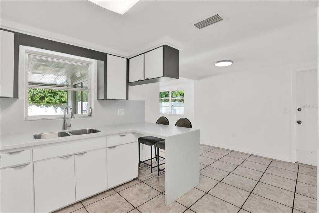 A kitchen with white cabinets, a peninsula, and tiled floors overlooks a dining area — 6701 PARKSIDE DRIVE, NEW PORT RICHEY, FL