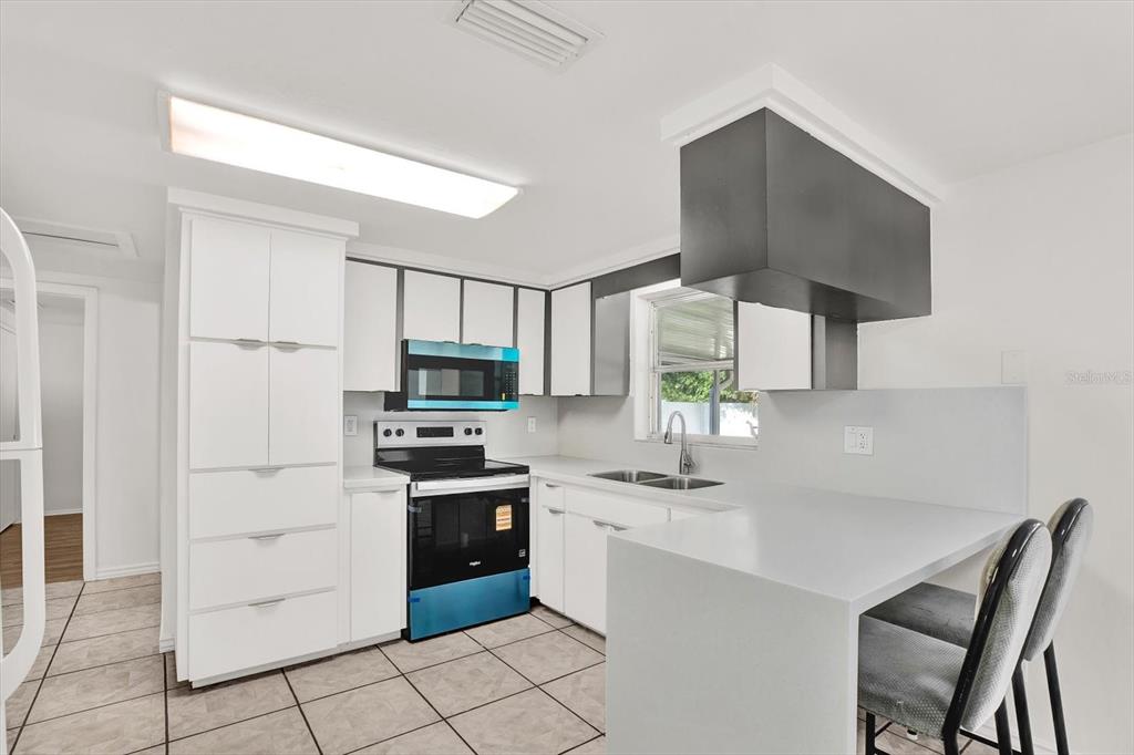 A kitchen features white cabinetry, a black range hood, stainless steel appliances, and tiled flooring — 6701 PARKSIDE DRIVE, NEW PORT RICHEY, FL