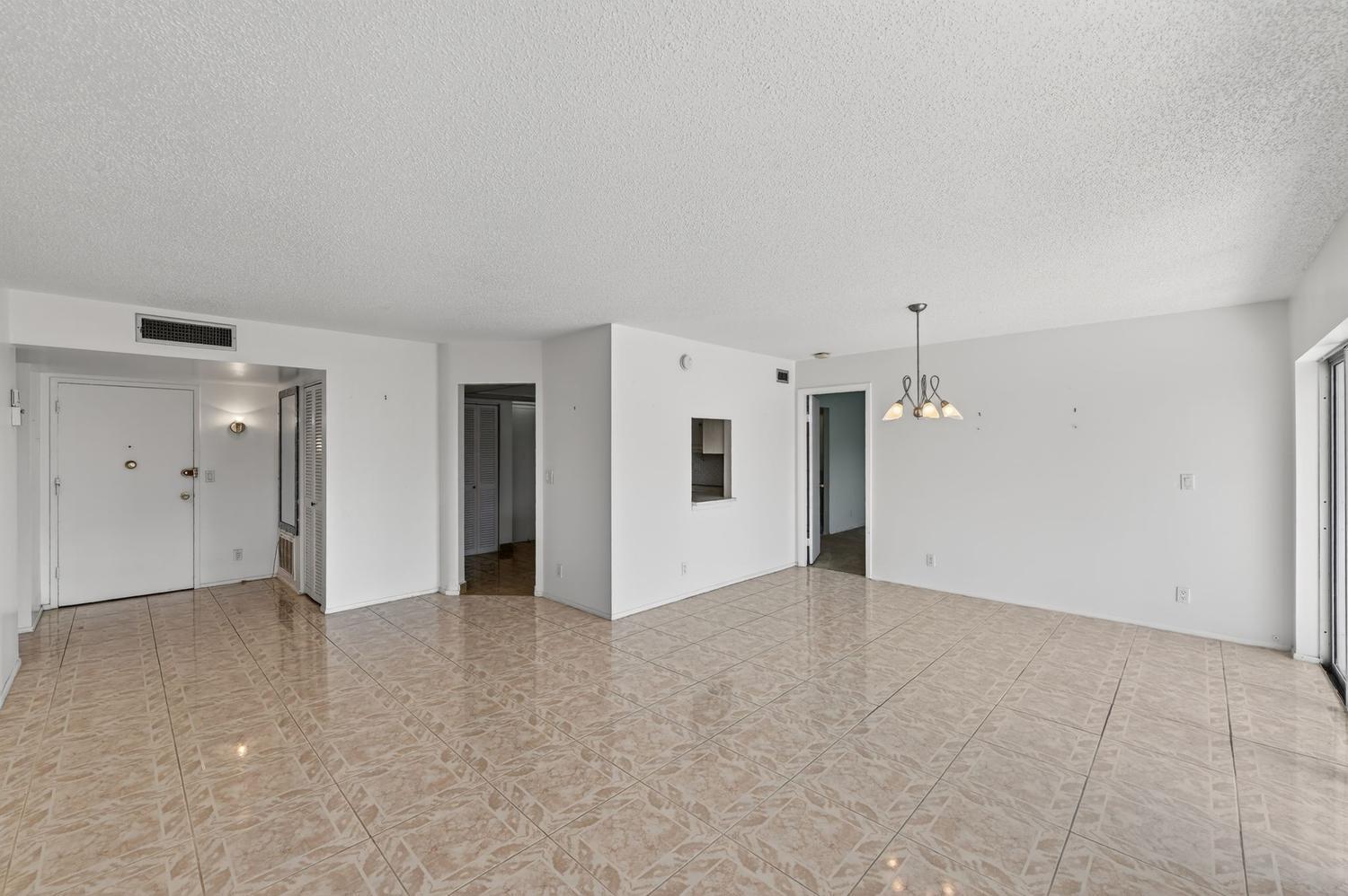 An empty living and dining area features white walls, a popcorn ceiling, and tiled floors — 400 Diplomat Parkway # 612, Hallandale Beach FL 33009, HALLANDALE BEACH, FL