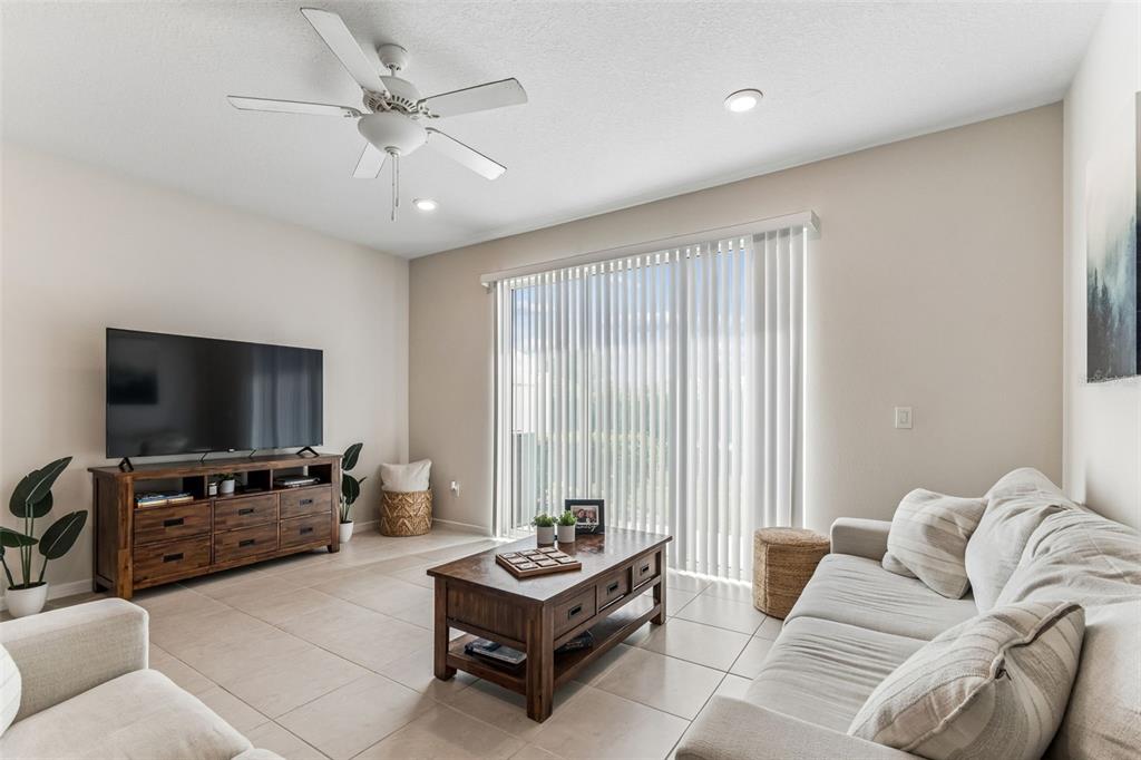 A living room features tile flooring, a ceiling fan, a television console, and a sofa — 31357 AMBERVIEW BEND, WESLEY CHAPEL, FL