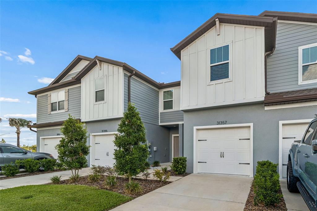 A row of two-story townhomes with gray siding, white board-and-batten accents, and attached garages — 31357 AMBERVIEW BEND, WESLEY CHAPEL, FL