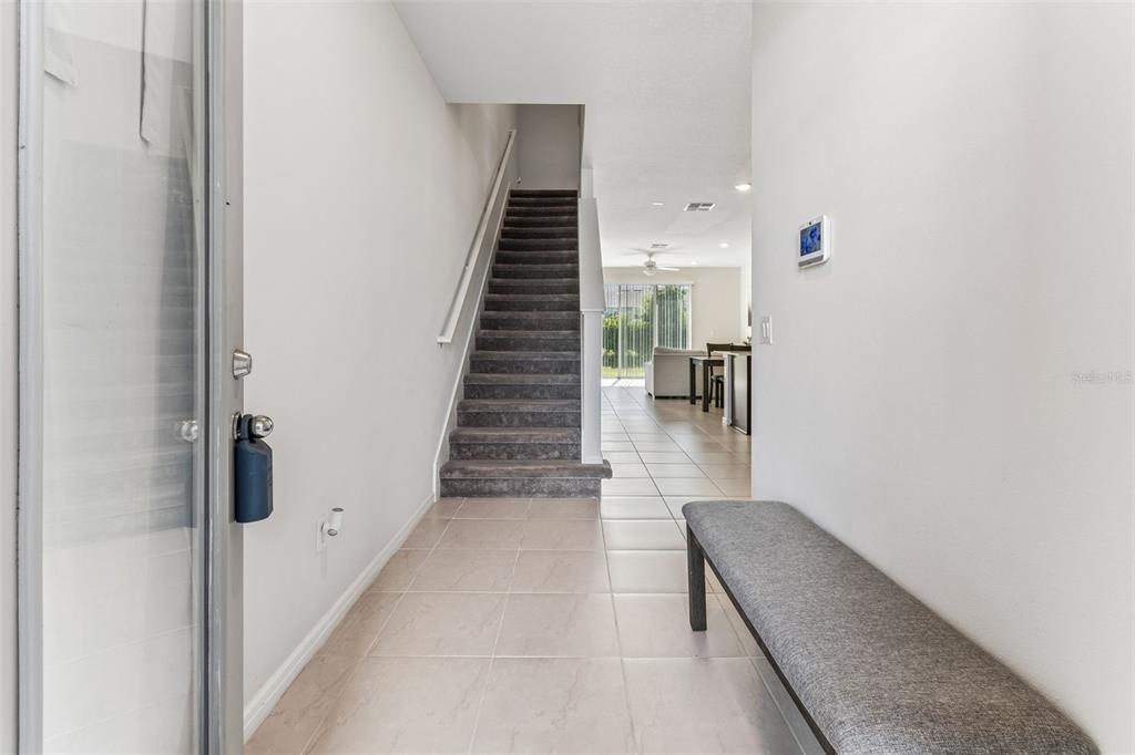 An entryway features a carpeted staircase, tiled flooring, a gray bench, and a view beyond — 31357 AMBERVIEW BEND, WESLEY CHAPEL, FL