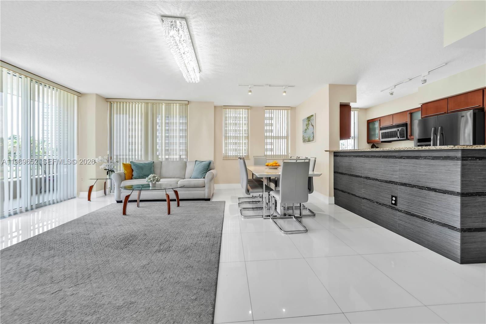 An open-concept living and dining area features white tile floors, a grey rug, and kitchen — 2080 S Ocean Dr # 202, Hallandale Beach FL 33009, HALLANDALE BEACH, FL