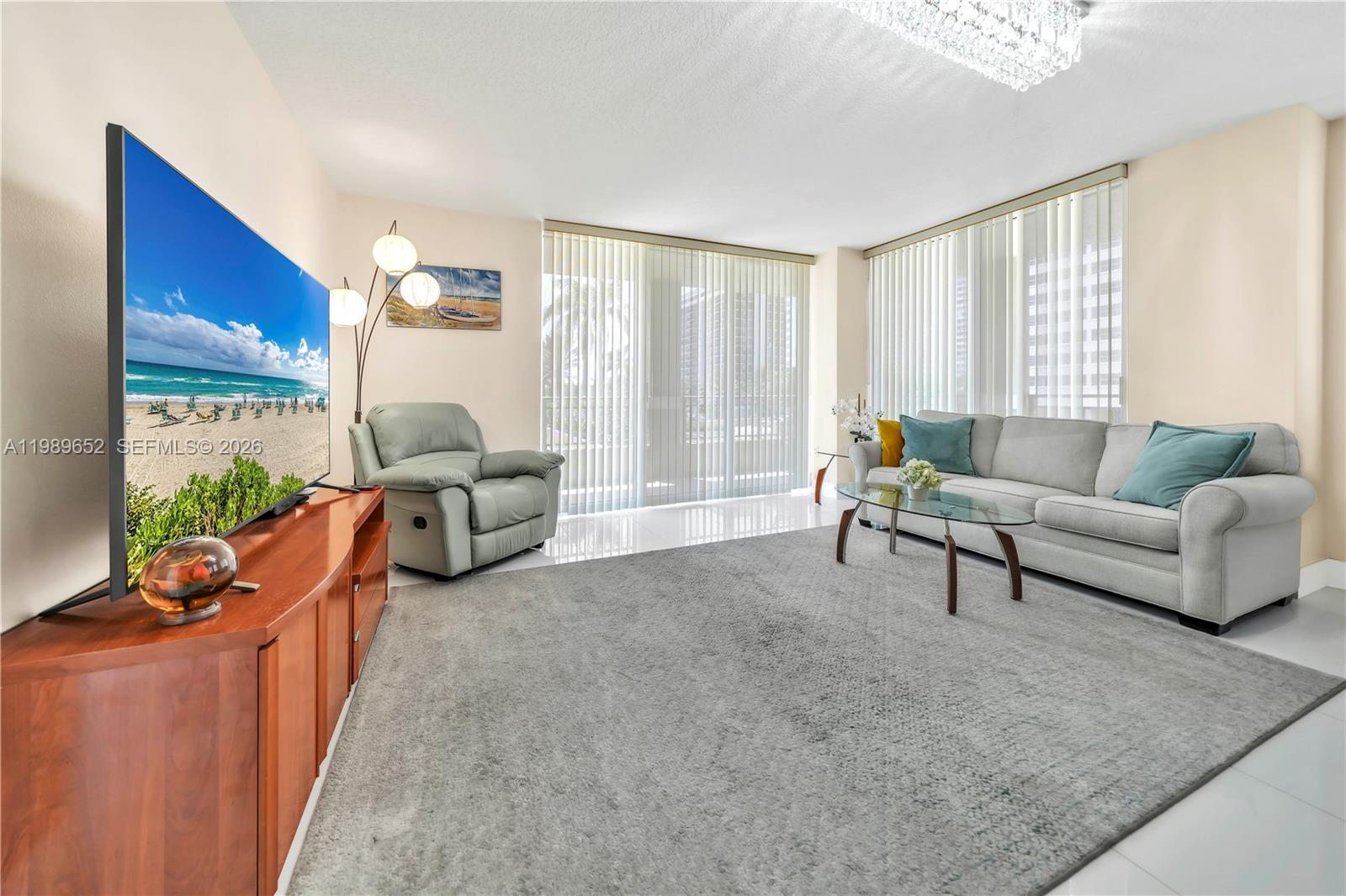A living room features a large television, a grey sofa, and a light-colored area rug — 2080 S Ocean Dr # 202, Hallandale Beach FL 33009, HALLANDALE BEACH, FL
