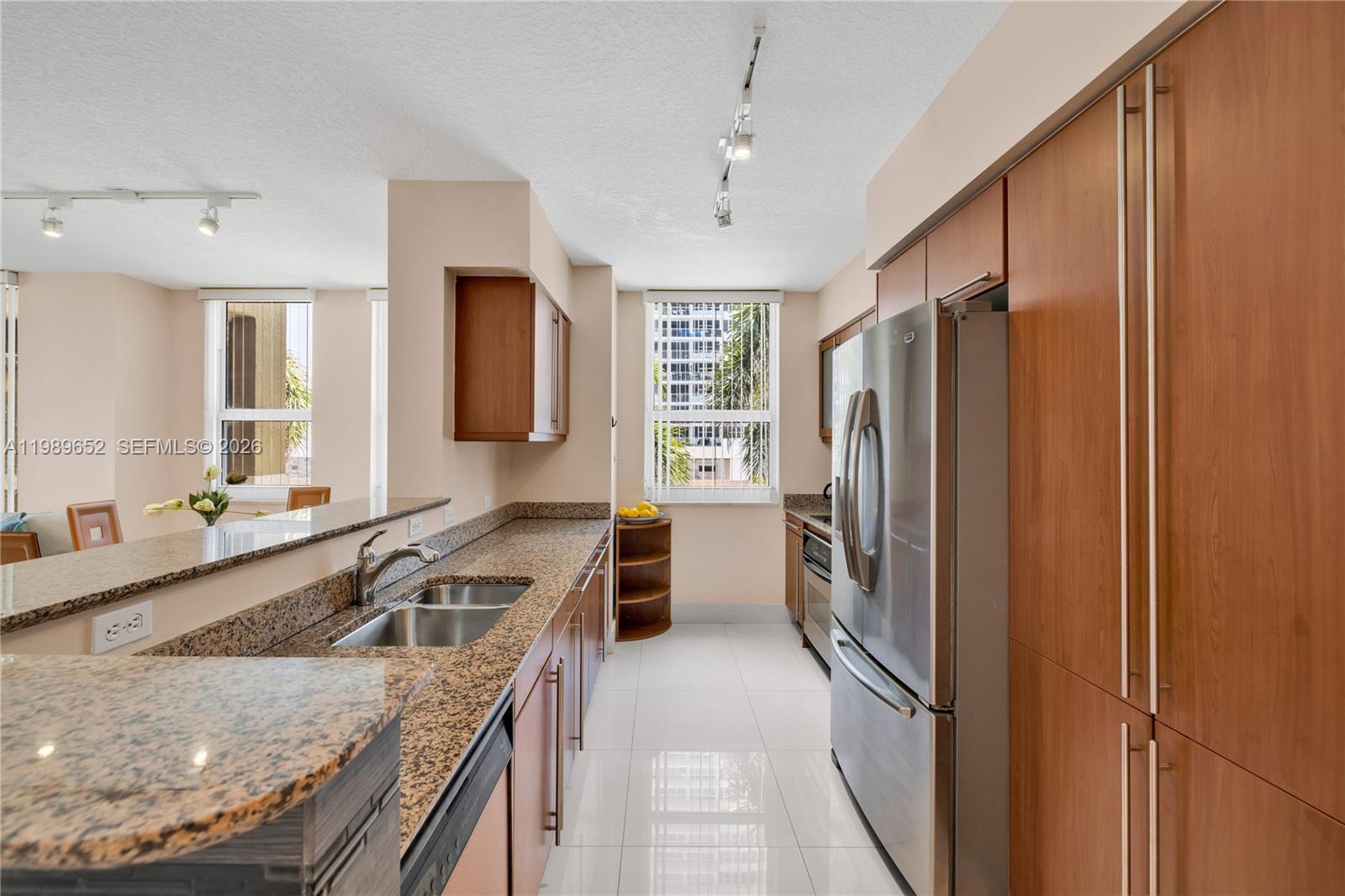 A kitchen features granite countertops, stainless steel appliances, and wood cabinetry on a white floor — 2080 S Ocean Dr # 202, Hallandale Beach FL 33009, HALLANDALE BEACH, FL