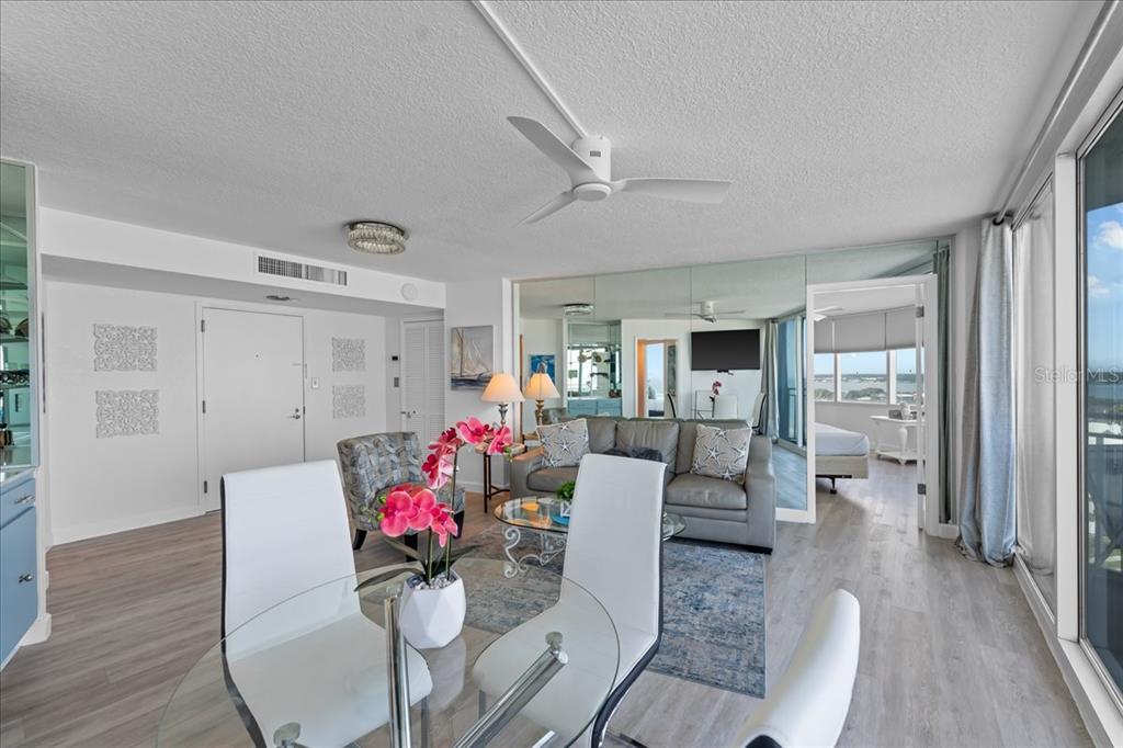 A bright living and dining area features white furniture, a glass table, and mirrored walls — 2625 S ATLANTIC AVENUE UNIT 11NW, DAYTONA BEACH, FL