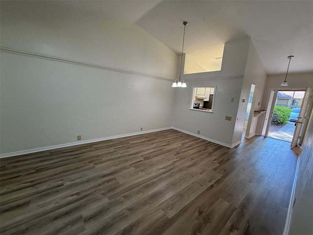 An empty living room with vaulted ceilings, wood-look flooring, and a pass-through to the kitchen — 4052 NW 23RD CIRCLE, GAINESVILLE, FL