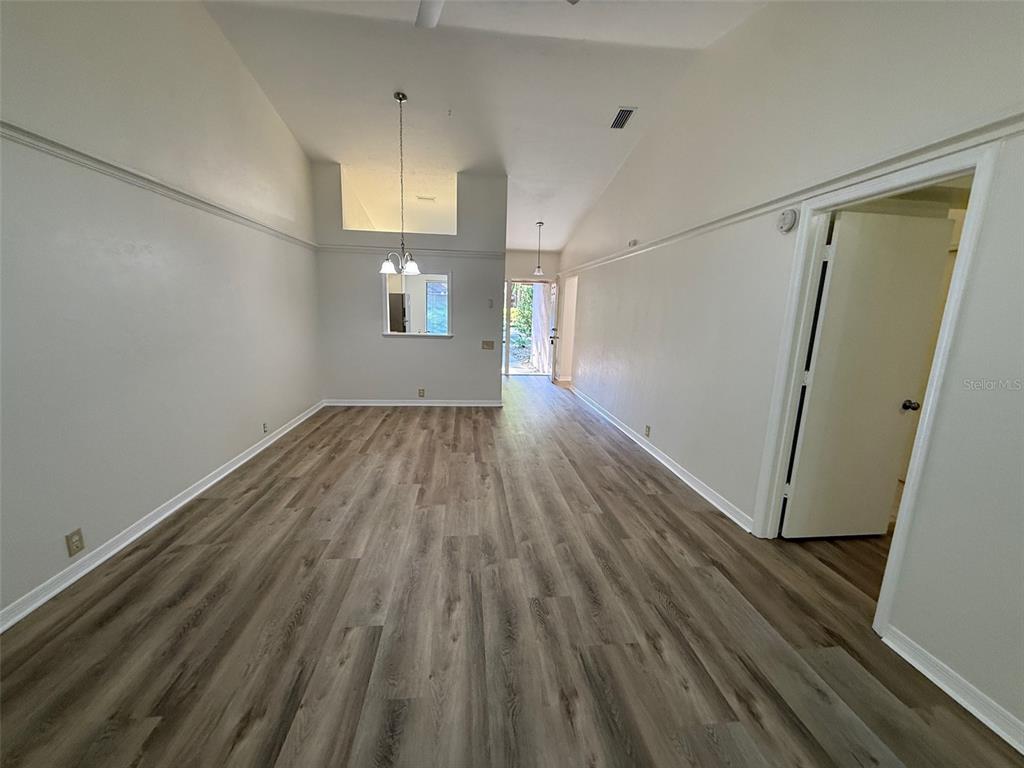 An empty room with vaulted ceilings, light-colored walls, and wood-look vinyl flooring — 4052 NW 23RD CIRCLE, GAINESVILLE, FL