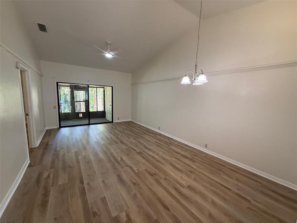 A living room with light wood-look flooring, a vaulted ceiling, and a sliding glass door — 4052 NW 23RD CIRCLE, GAINESVILLE, FL