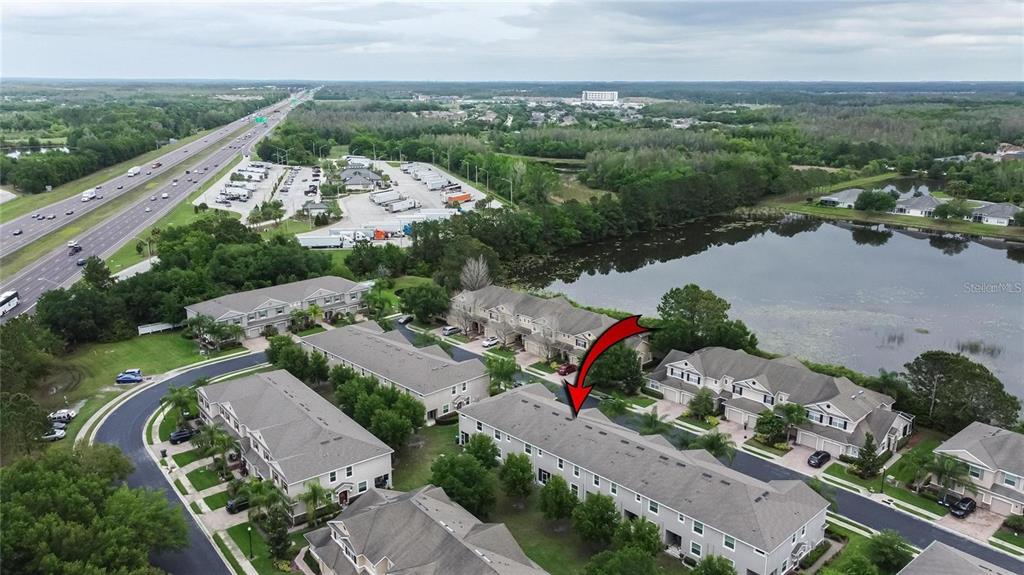 An aerial view shows a multi-story townhouse complex situated next to a lake and highway — 3903 SILVERLAKE WAY, WESLEY CHAPEL, FL