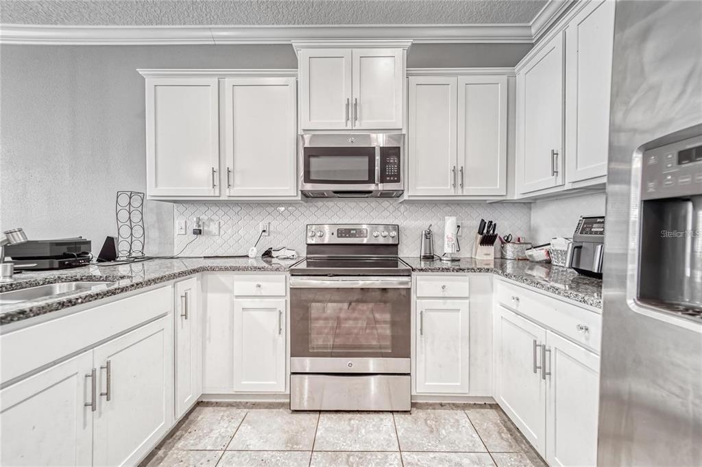 A kitchen features white cabinets, stainless steel appliances, and granite countertops with a tiled backsplash — 3903 SILVERLAKE WAY, WESLEY CHAPEL, FL