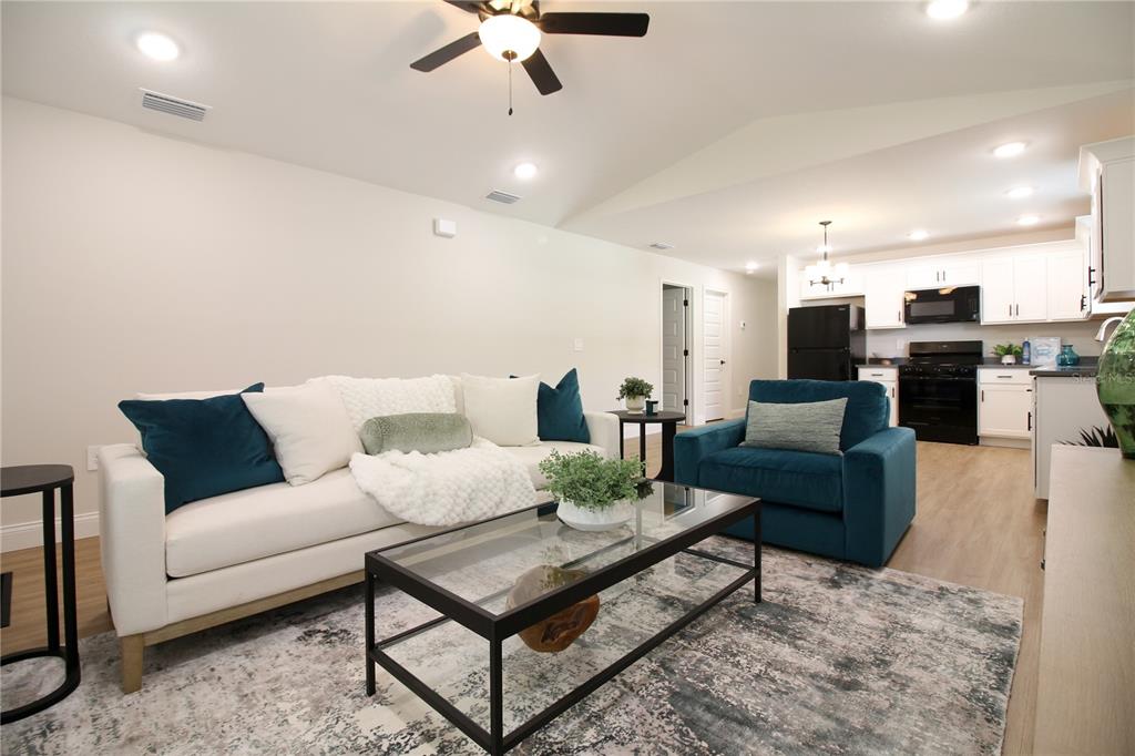A living room with a white sofa and blue armchair opens into a kitchen with white cabinets — 1242 DOROTHY STREET, LAKELAND, FL
