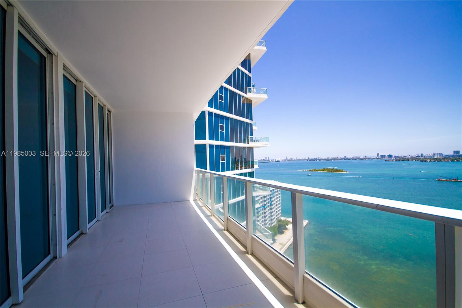 A balcony with white tile flooring and a glass railing overlooks a bay and city — 2020 N Bayshore Dr # 2204, Miami FL 33137, MIAMI, FL
