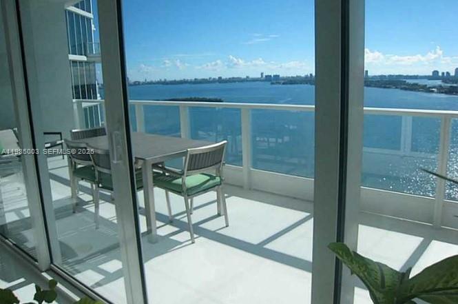 A balcony with a dining set overlooks a large body of water and a distant skyline — 2020 N Bayshore Dr # 2204, Miami FL 33137, MIAMI, FL
