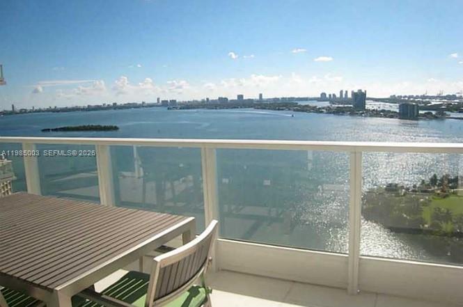 A balcony with a wooden table and chairs overlooks a large bay and city skyline — 2020 N Bayshore Dr # 2204, Miami FL 33137, MIAMI, FL