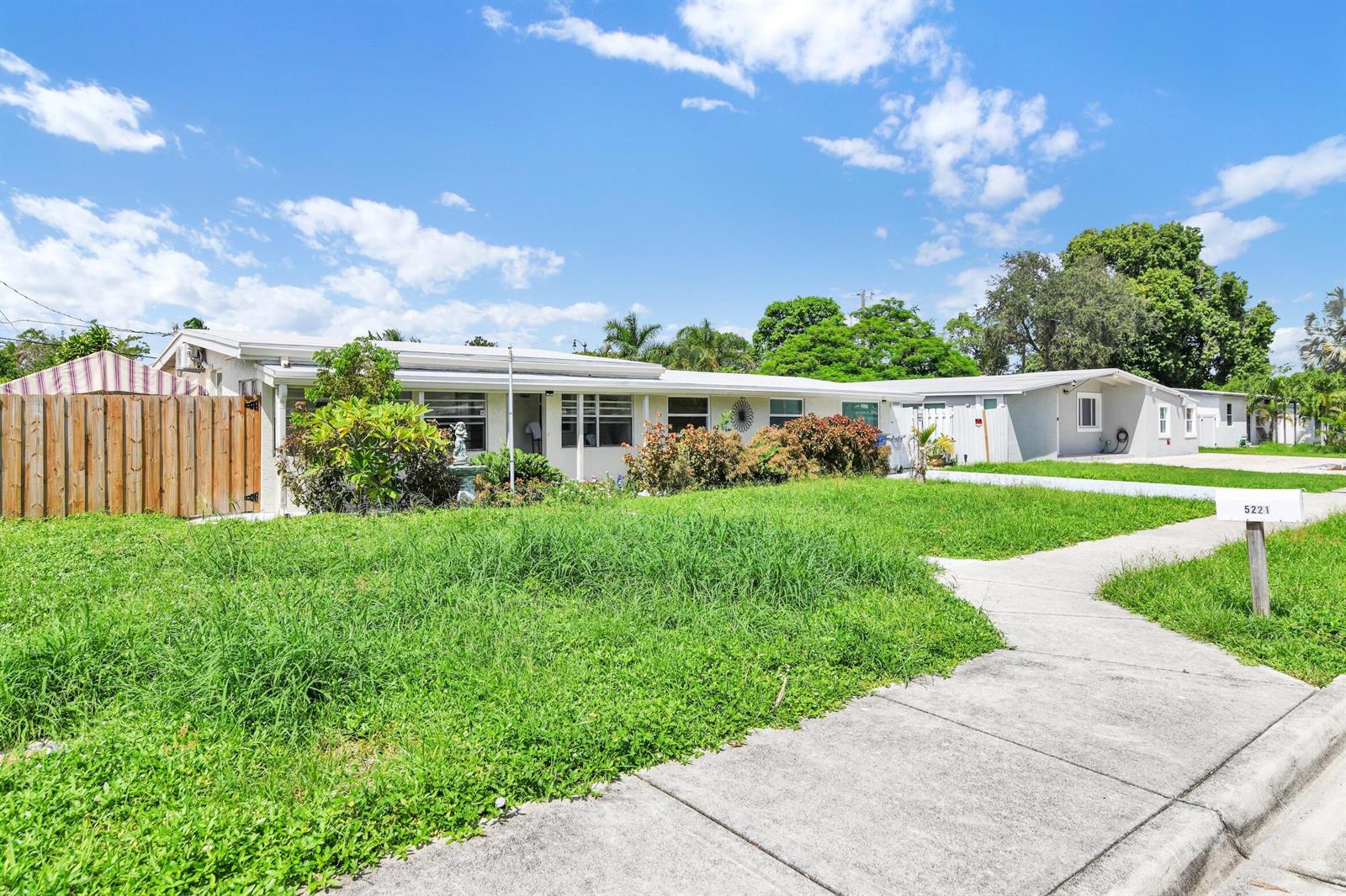 A single-story house with a wooden fence and a lawn under a blue sky — 5221 NE 16th Avenue, Pompano Beach FL 33064, POMPANO BEACH, FL