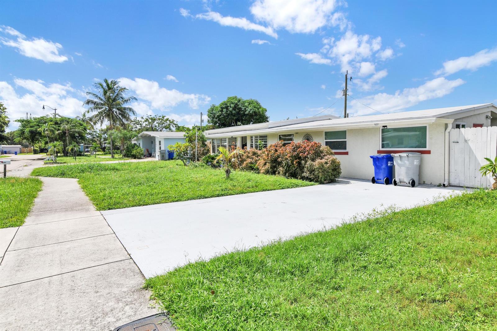 A single-story house with a white concrete driveway, a front lawn, and two trash bins — 5221 NE 16th Avenue, Pompano Beach FL 33064, POMPANO BEACH, FL