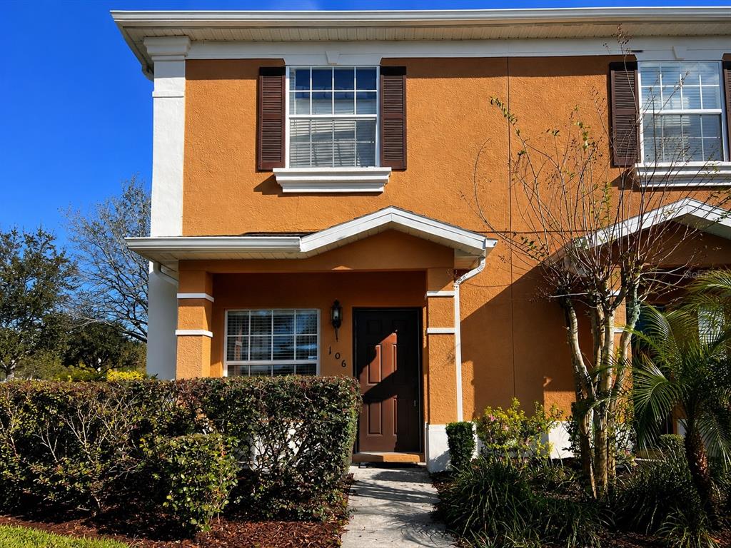 A two-story orange stucco townhouse with brown shutters, a covered entryway, and a front hedge — 106 WEYMOUTH DRIVE, DAVENPORT, FL