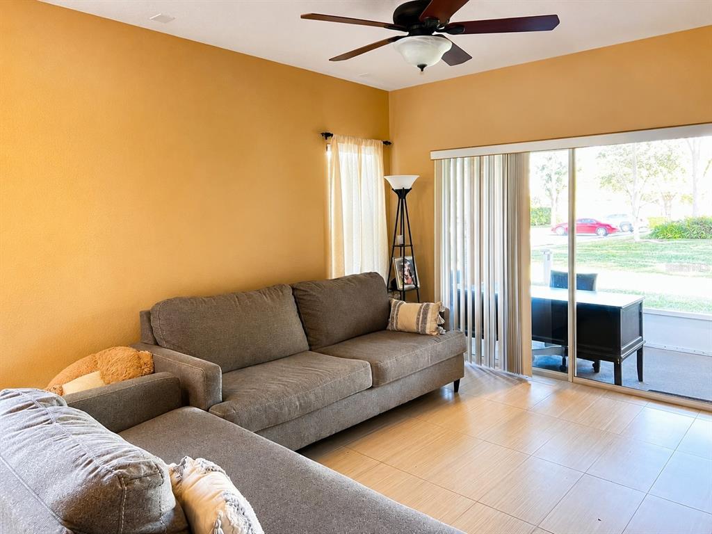A living room with a grey sectional sofa, tile flooring, and a sliding glass door — 106 WEYMOUTH DRIVE, DAVENPORT, FL
