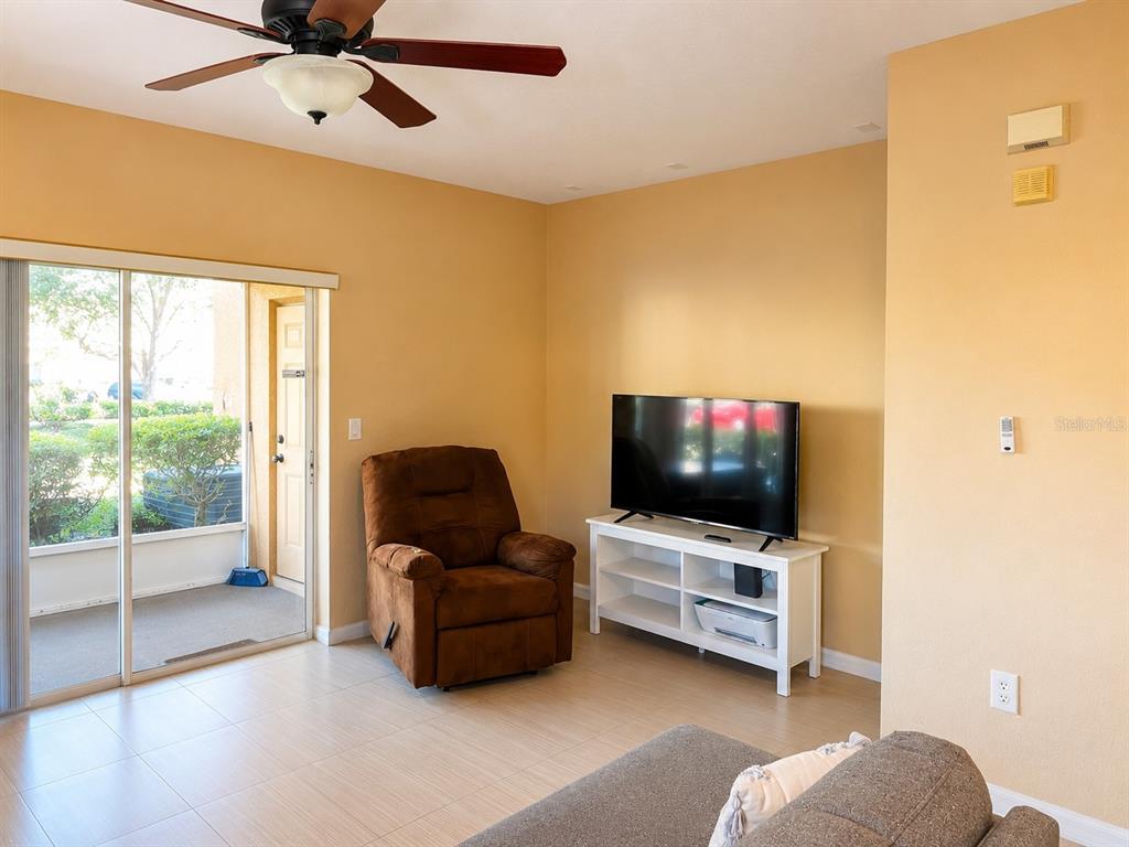 A living room features a brown recliner, a television on a white stand, and sliding doors — 106 WEYMOUTH DRIVE, DAVENPORT, FL