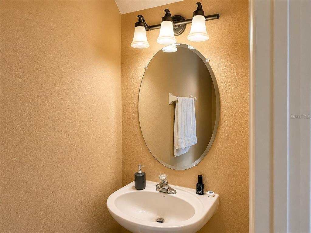 A small bathroom features a wall-mounted sink, an oval mirror, and a three-light vanity fixture — 106 WEYMOUTH DRIVE, DAVENPORT, FL