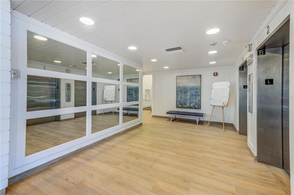 A bright elevator lobby features wood-look flooring, a mirrored wall, and two metal elevator doors — 7100 SUNSET WAY UNIT 310, ST PETE BEACH, FL
