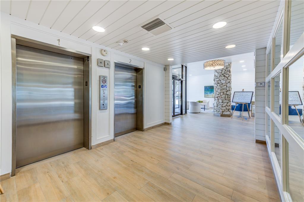 An elevator lobby features two stainless steel doors, wood-look flooring, and a stone-clad pillar — 7100 SUNSET WAY UNIT 310, ST PETE BEACH, FL