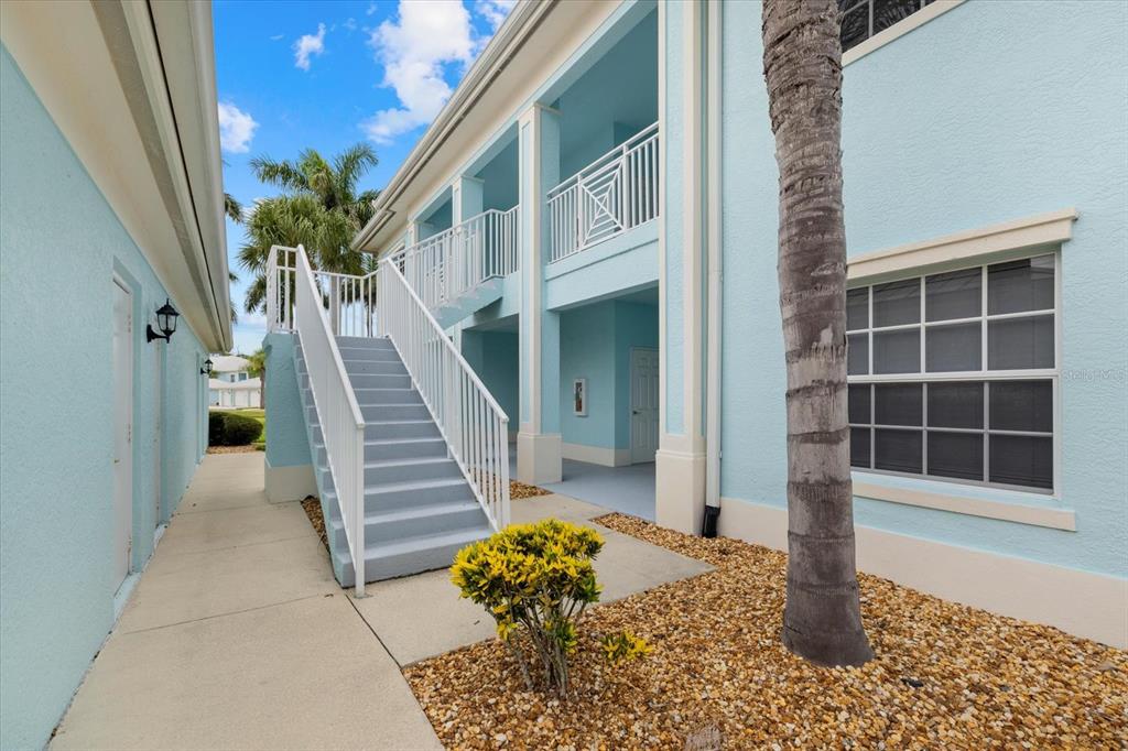 An exterior view of a light blue two-story building with an outdoor staircase and landscaping — 5738 SABAL TRACE DRIVE UNIT 1B5738, NORTH PORT, FL