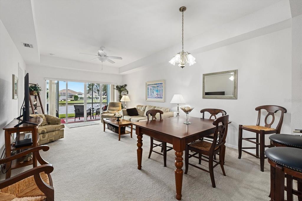 A living and dining area with carpeted floors, a wooden table, and sliding glass doors — 5738 SABAL TRACE DRIVE UNIT 1B5738, NORTH PORT, FL